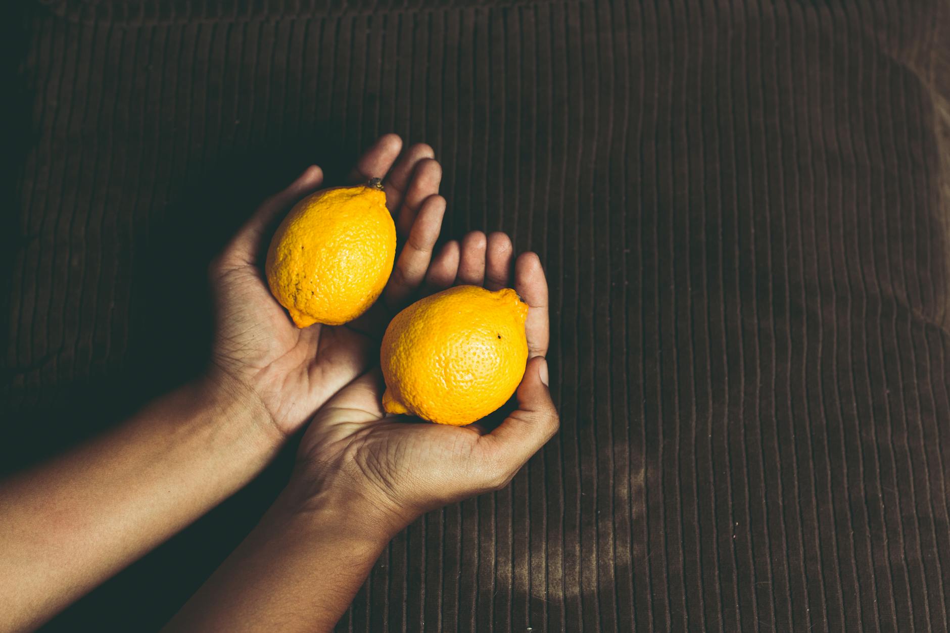 Foto de dos manos sosteniendo un limón fresco sobre una superficie marrón, simbolizando frescura e intimidad.