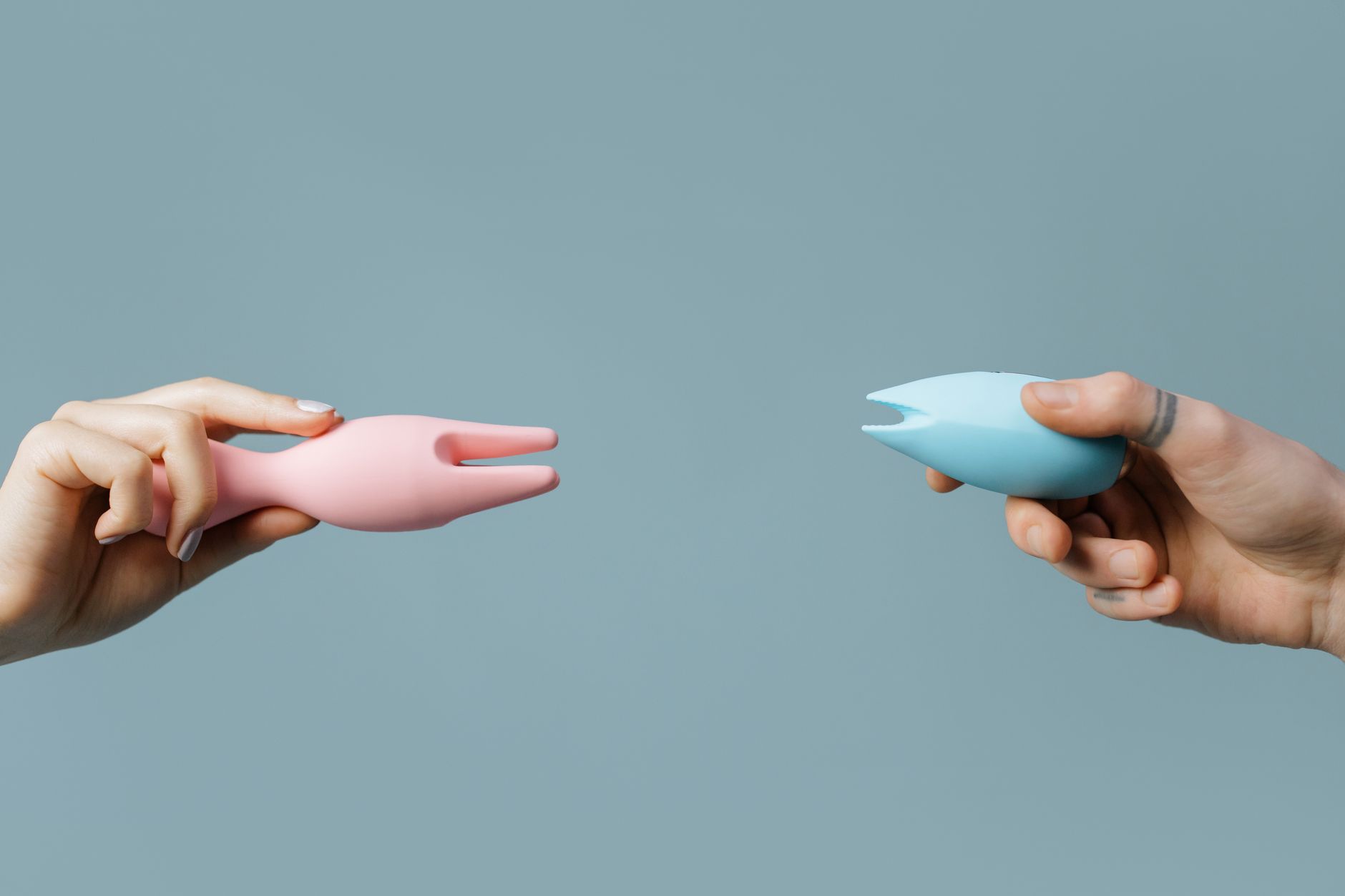 Hands holding pastel-colored silicone vibrators against a soft background.