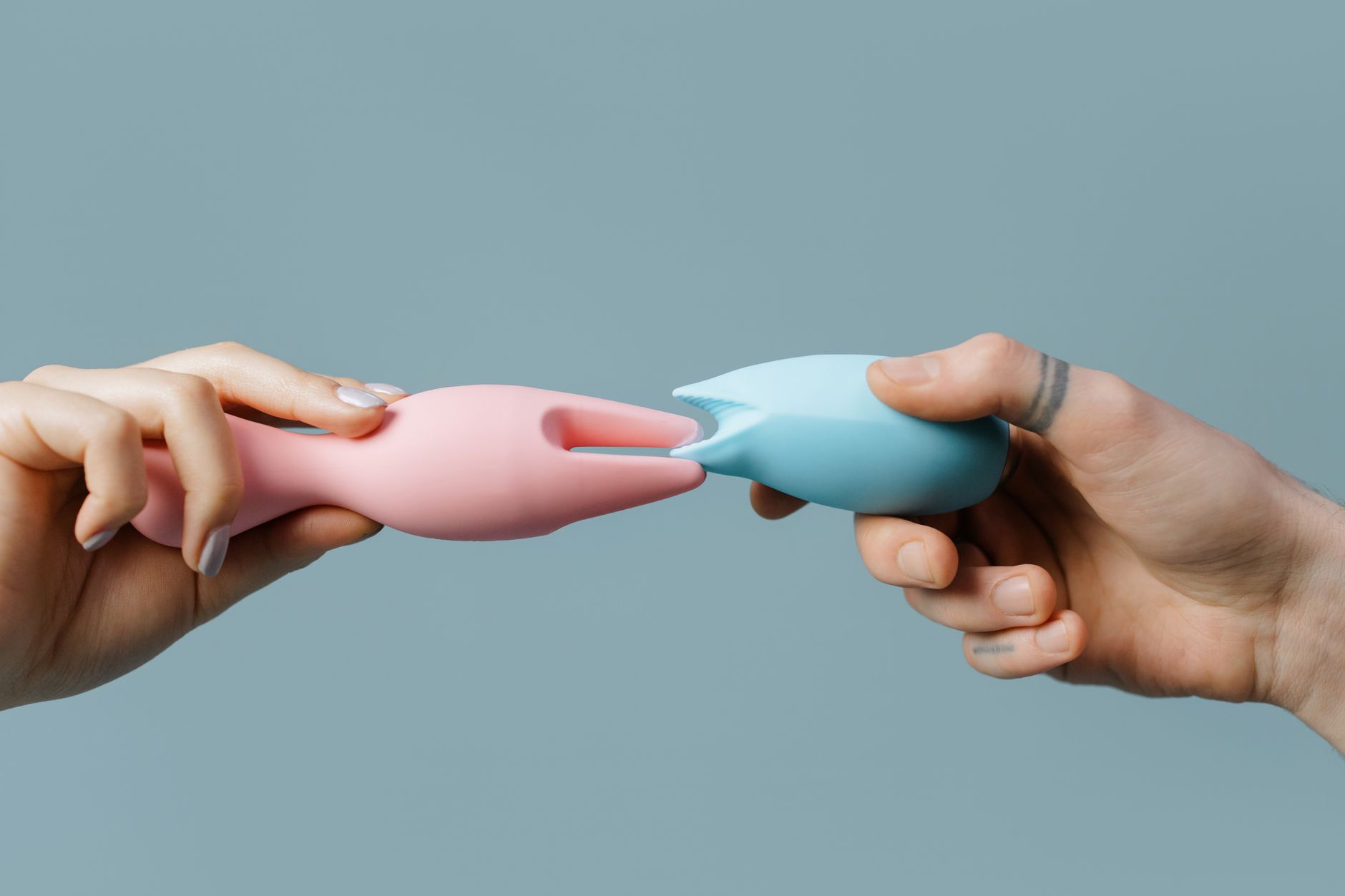 Two hands holding pink and blue silicone vibrators against a pastel background, representing options for sensation recovery