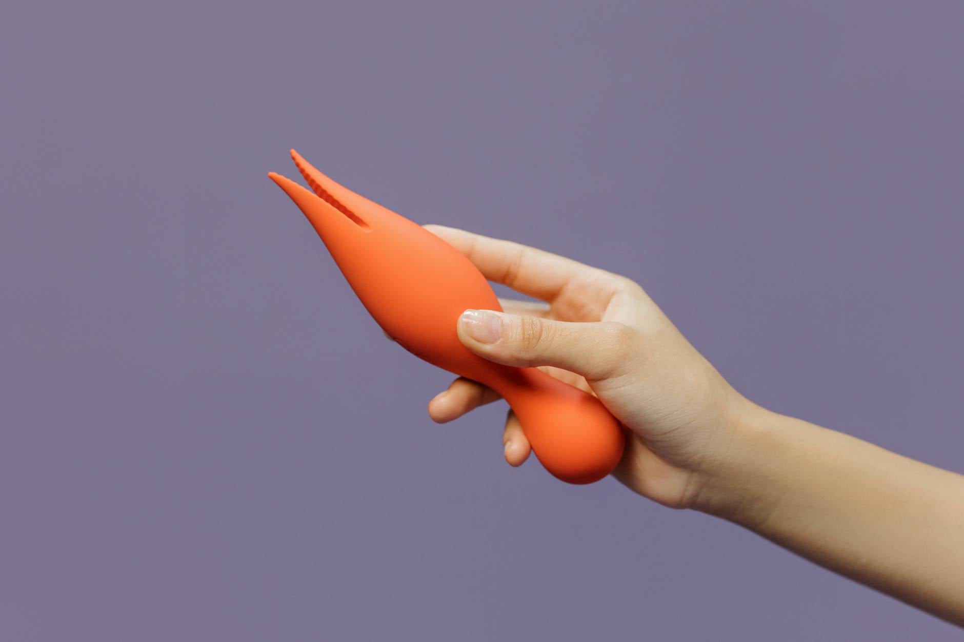 A hand holding an orange vibrator against a minimalistic purple backdrop, showcasing modern sensuality