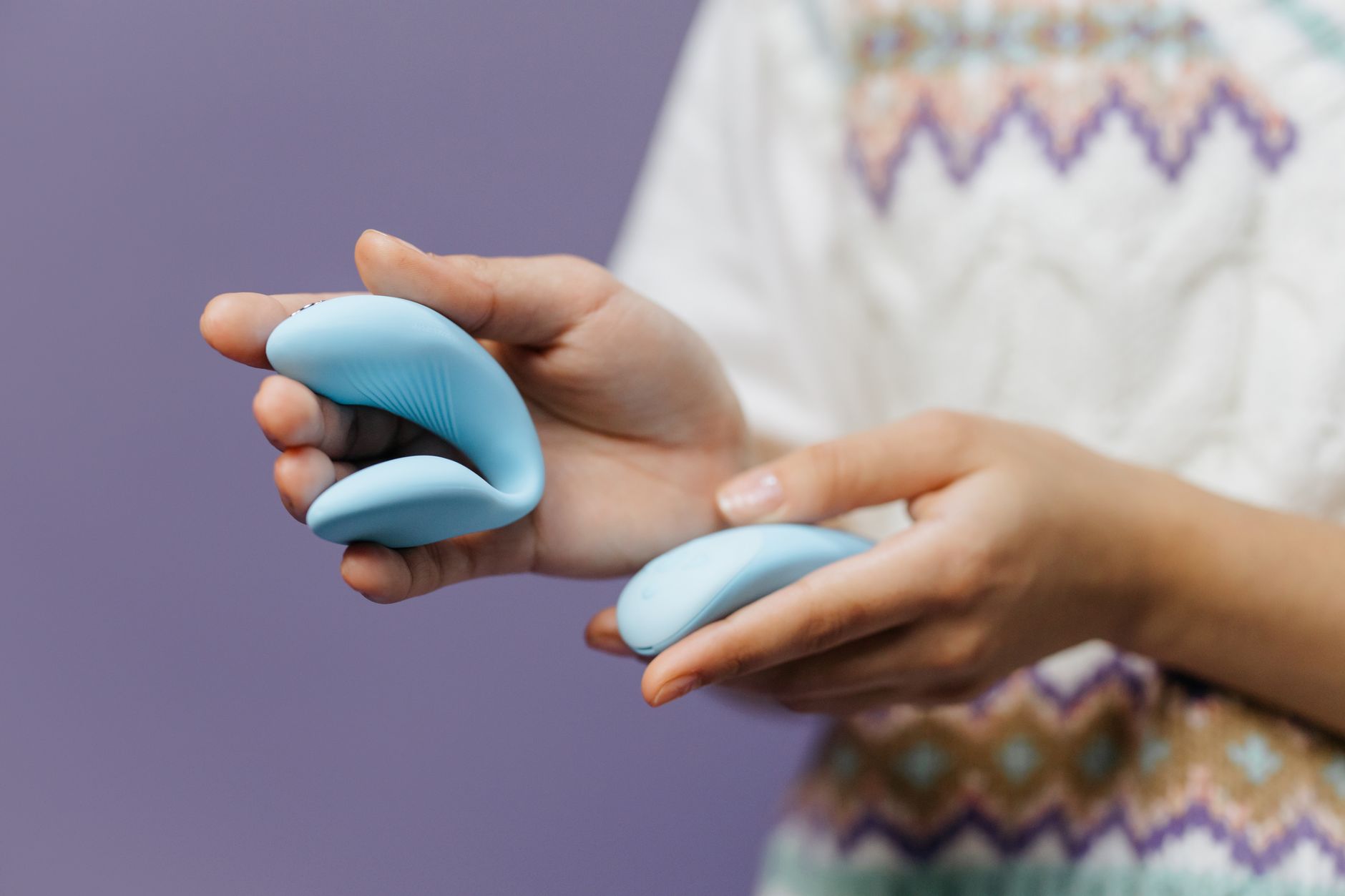Close-up of hands holding a sleek blue vibrator against a purple background