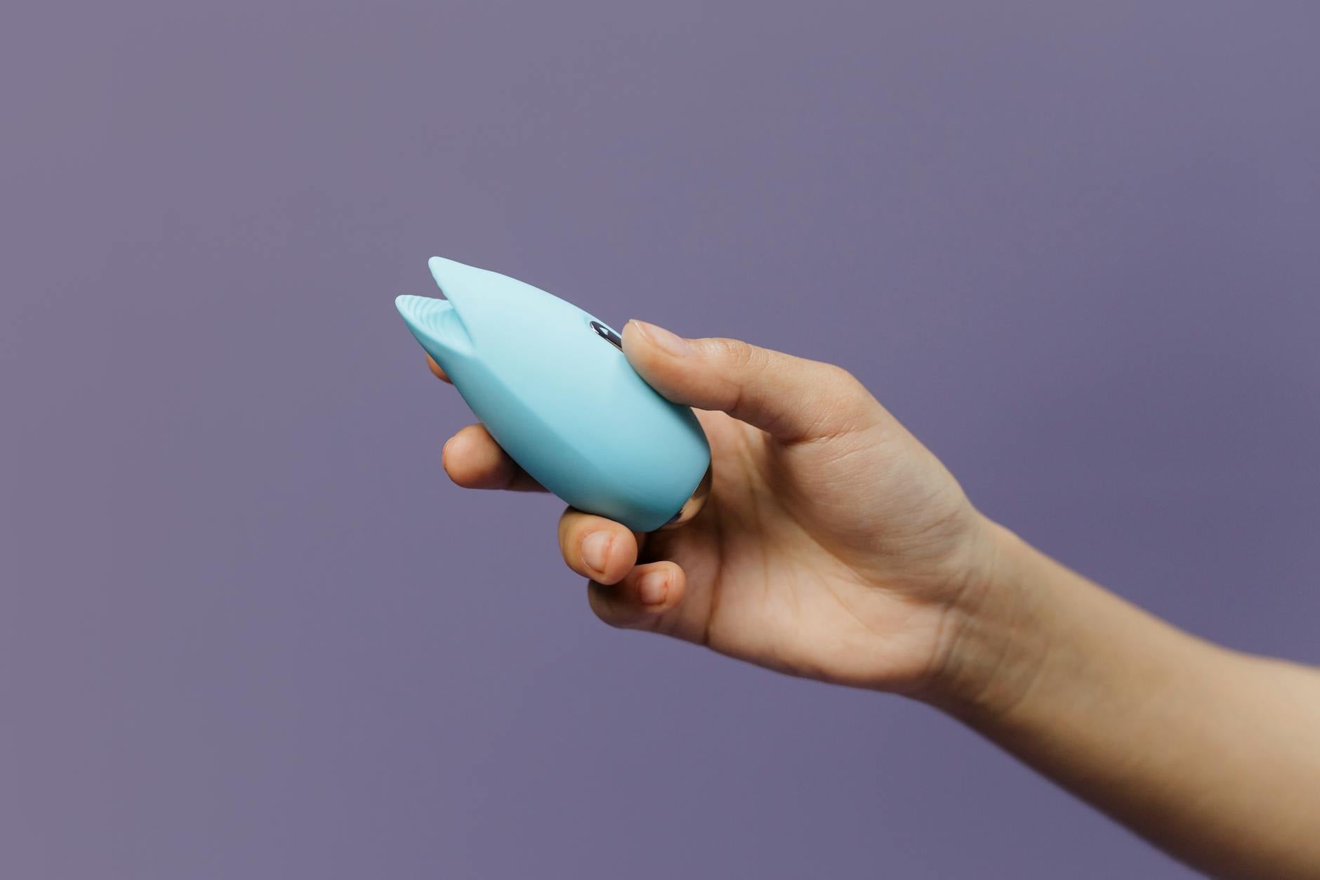 A vibrant blue silicone clitoral vibrator held in hand, symbolizing intimacy and self-care.