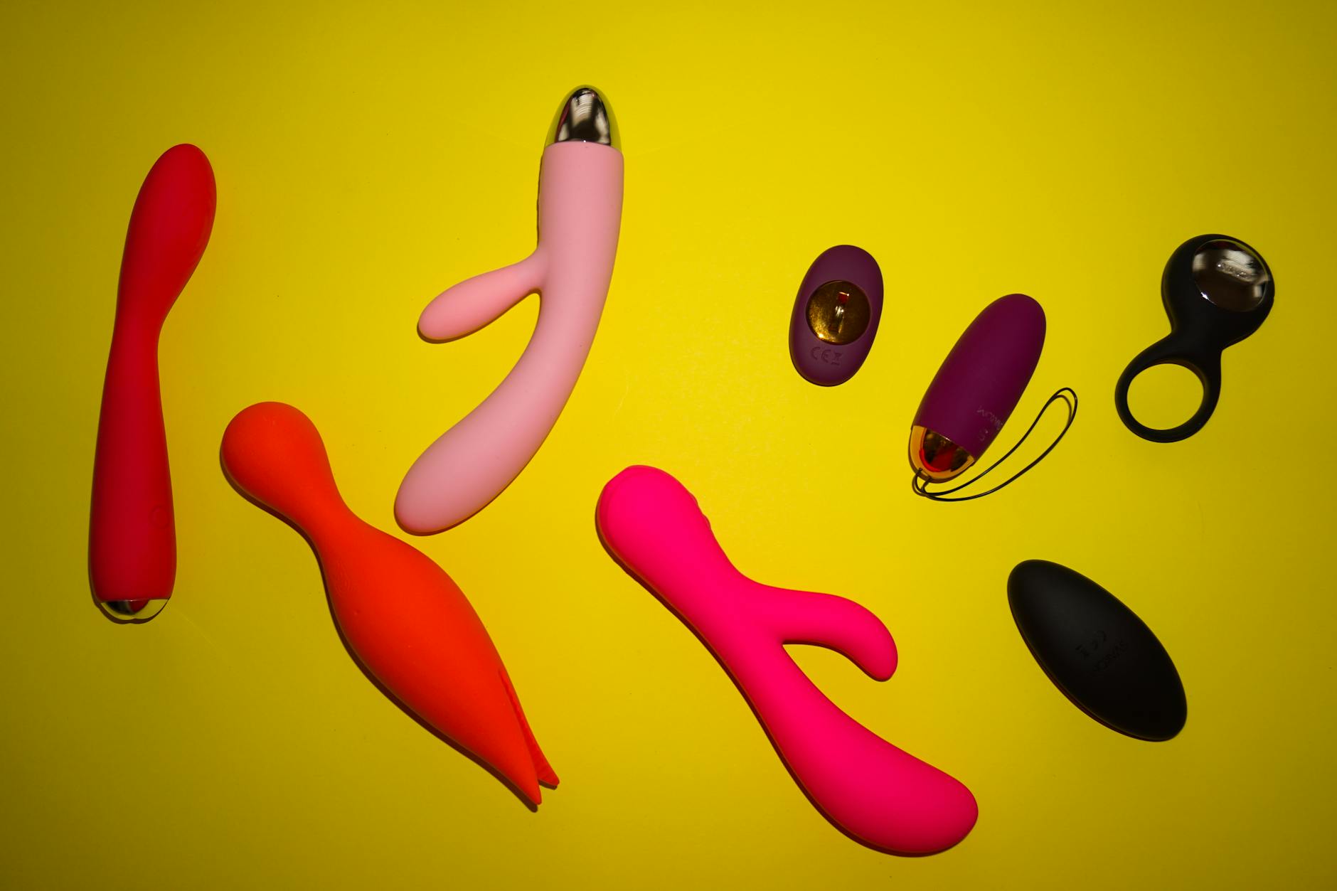 Vibrant collection of colorful sex toys arranged on a bright yellow surface showcasing design and variety.