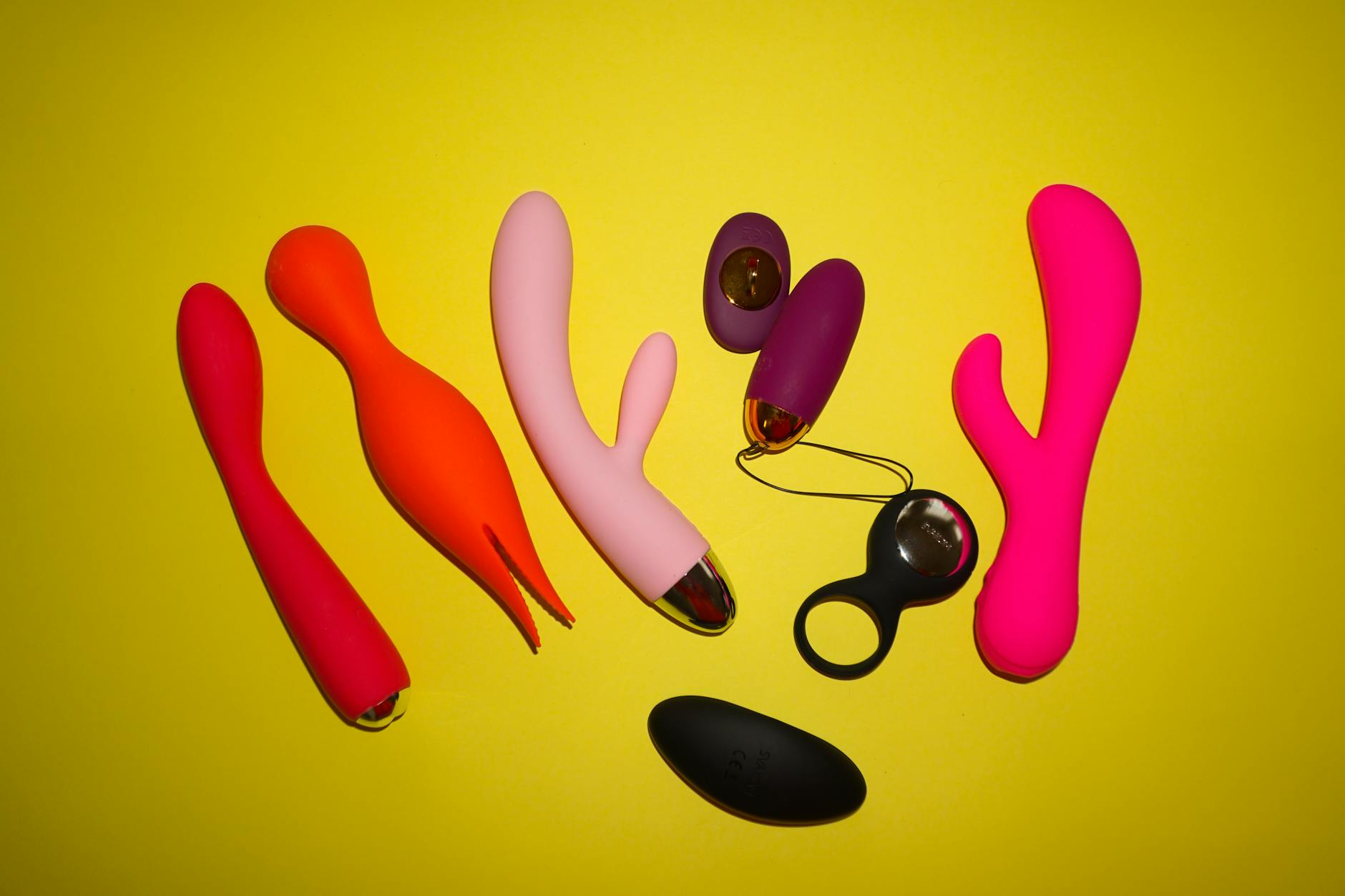Colorful adult toys arranged on a bright yellow background, showcasing shapes and texture variety