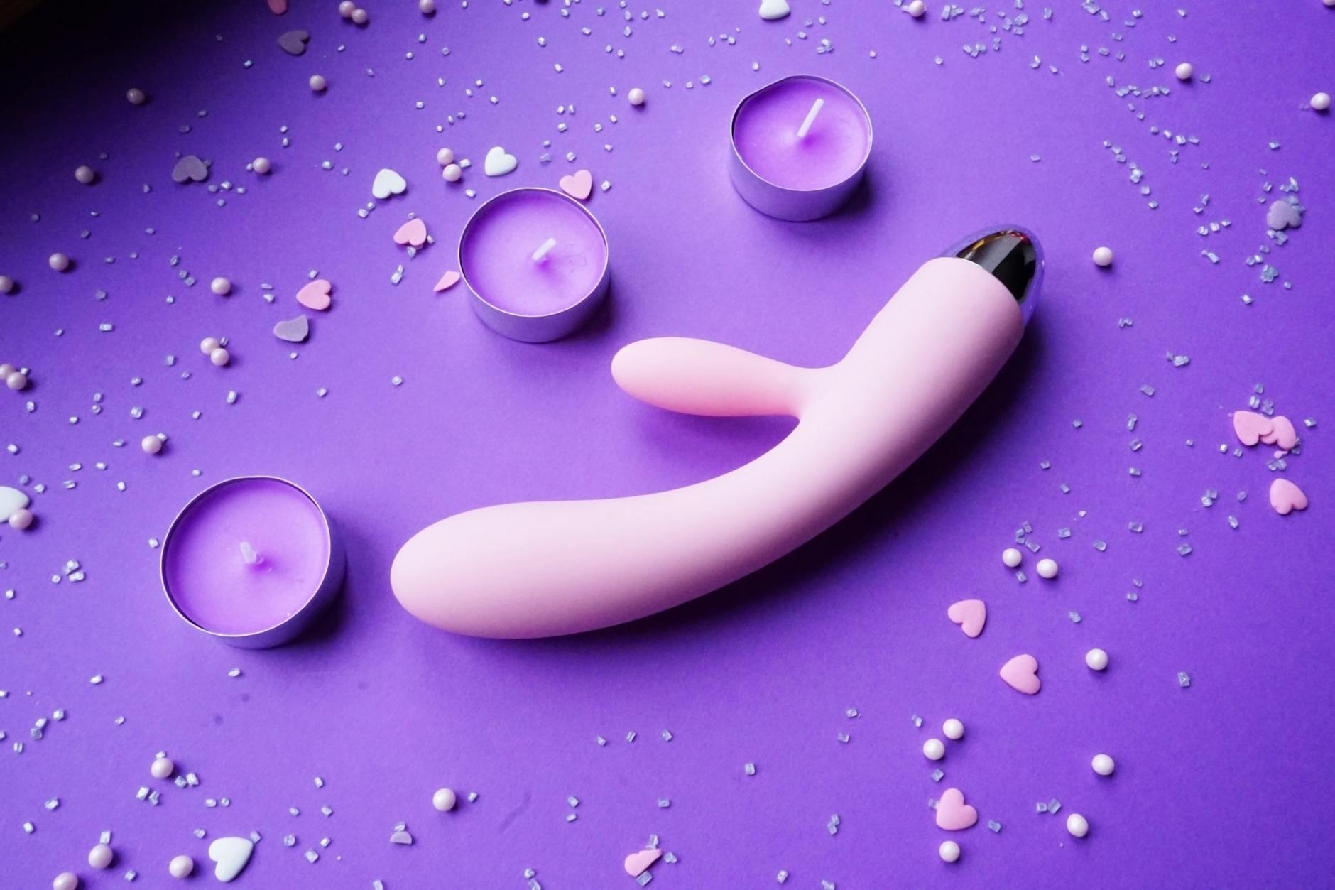Pink lemon vibrator on purple background with heart confetti and candles for intimate setting
